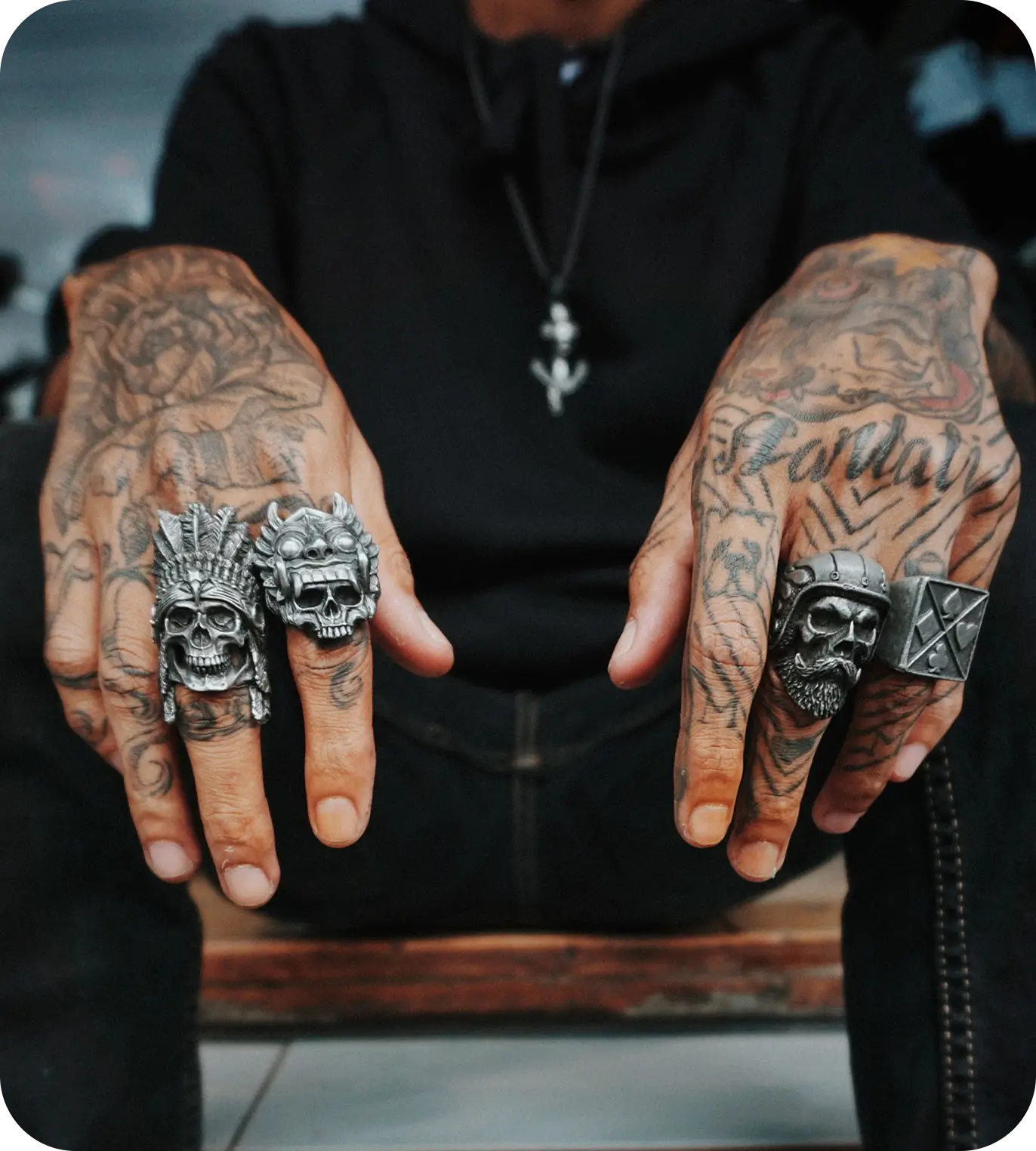 Tattooed hands wearing large skull rings.