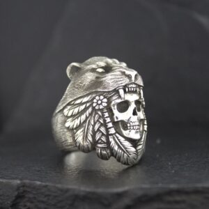 A silver ring featuring a bear and a skull with feathers design.