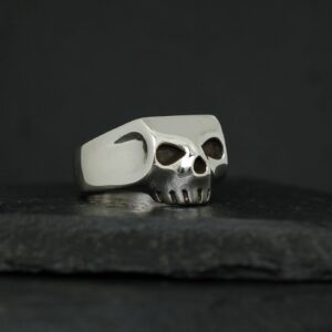 Silver skull ring with black eye sockets on a dark surface.