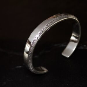 Silver cuff bracelet with intricate engravings on a dark background.