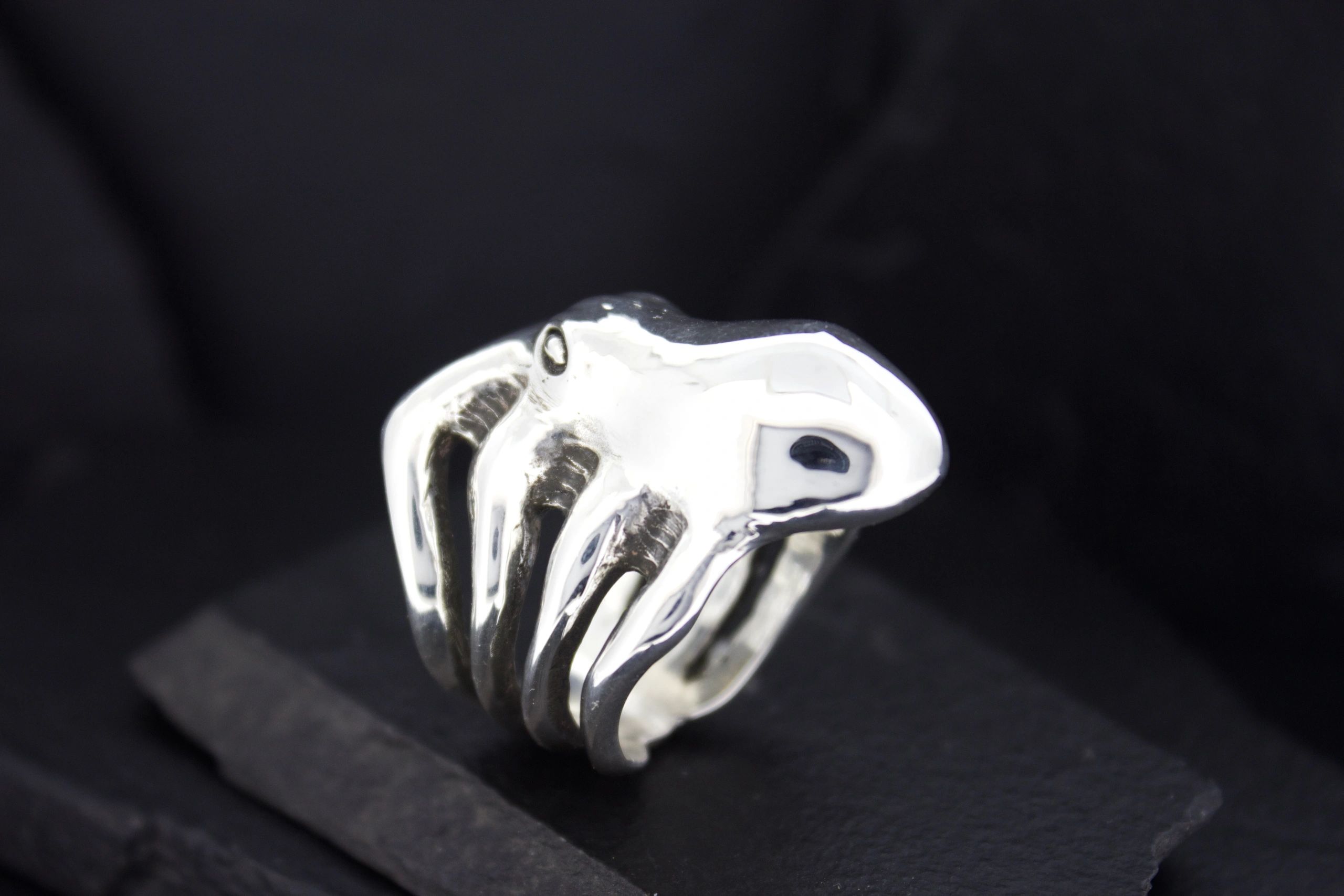 A sleek silver ring shaped like a skeletal hand on black background.
