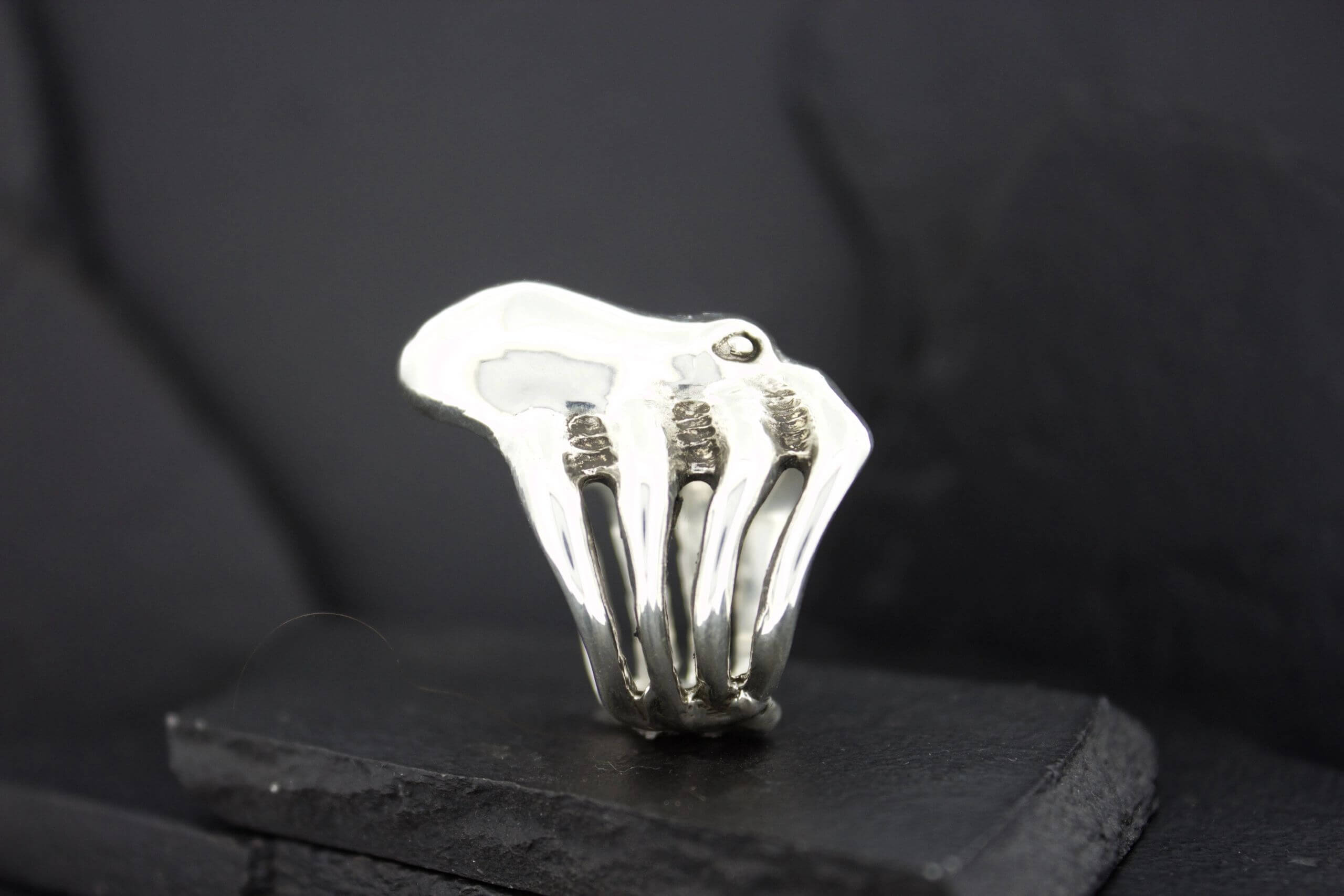 Silver ring shaped like a hand skeleton on a black surface.