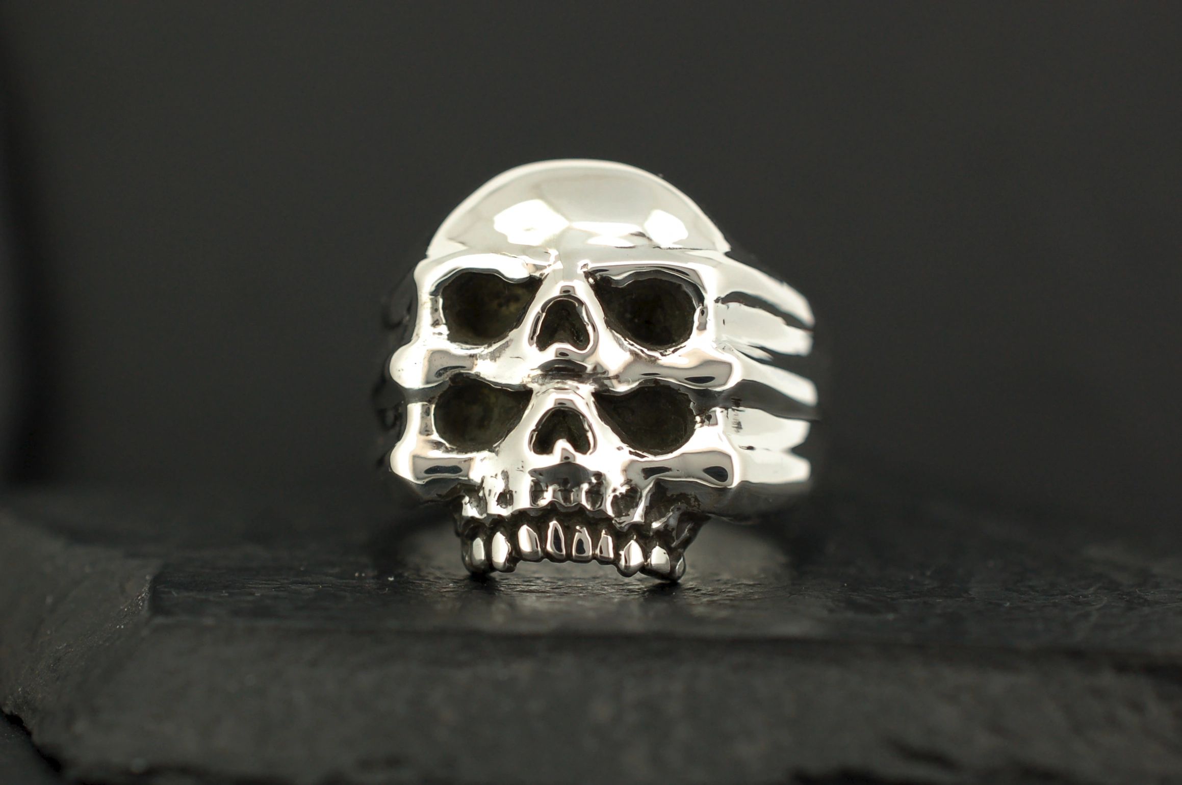 A silver skull-shaped ring with detailed features on a dark background.