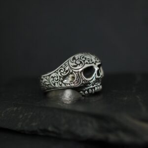 Intricately designed silver skull ring with detailed engravings on a dark background.