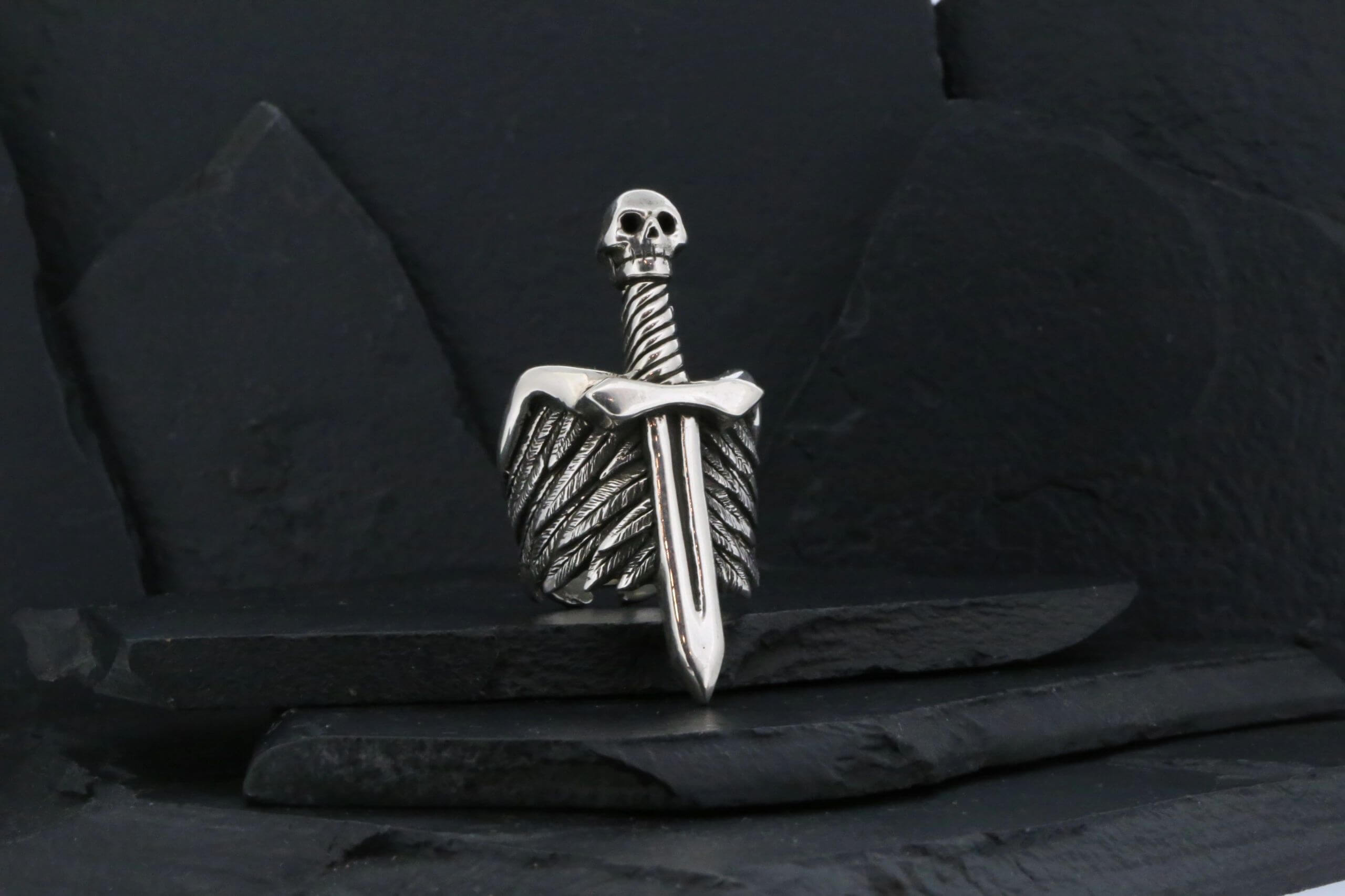 A silver dagger with a skull-shaped handle on a dark background.