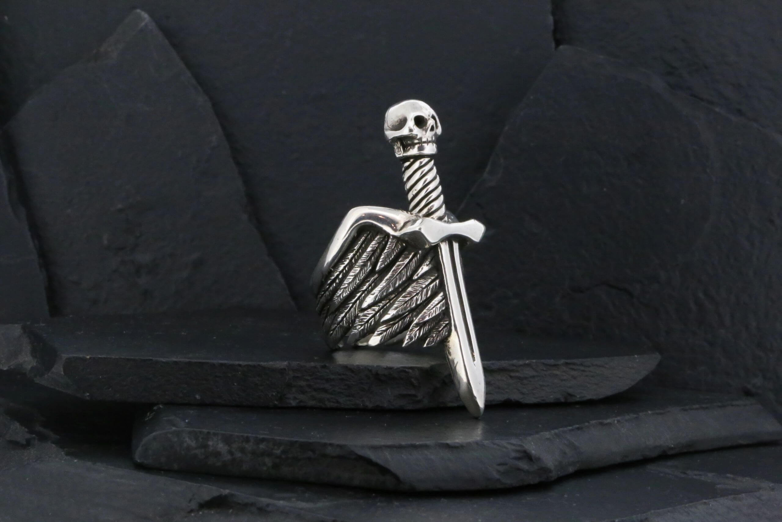 Silver skull and sword ring with intricate wing design.