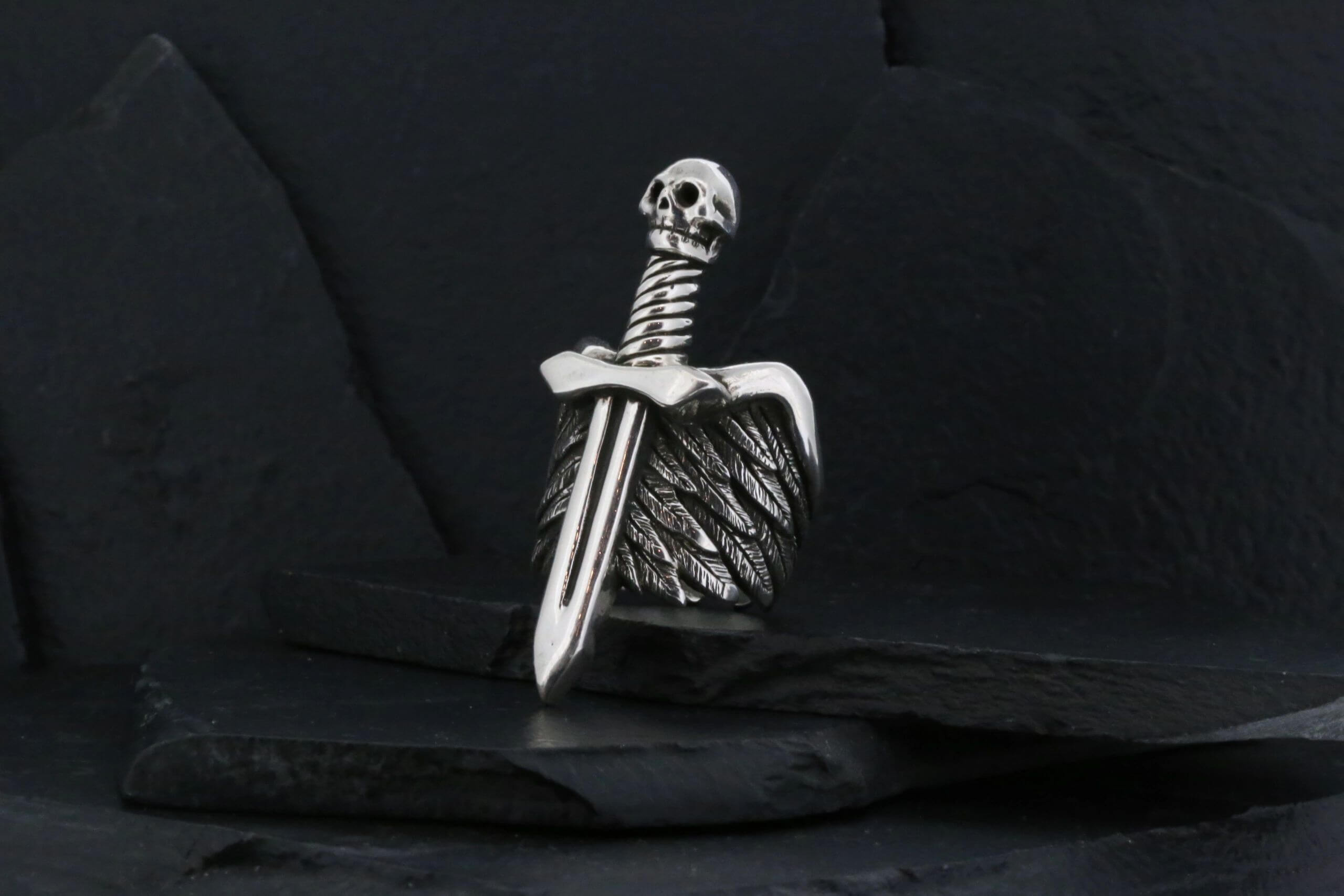 A silver sword pendant with detailed wings on a black background.