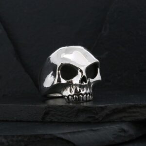 A shiny silver skull ring on a dark surface.
