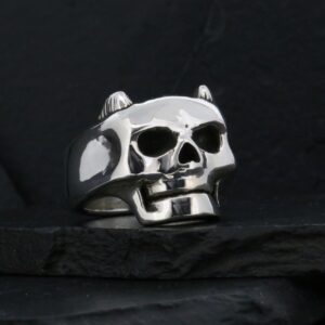 A metallic skull ring with intricate details on a dark background.