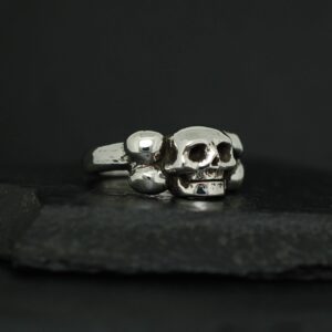 Two silver skull rings on a dark surface.
