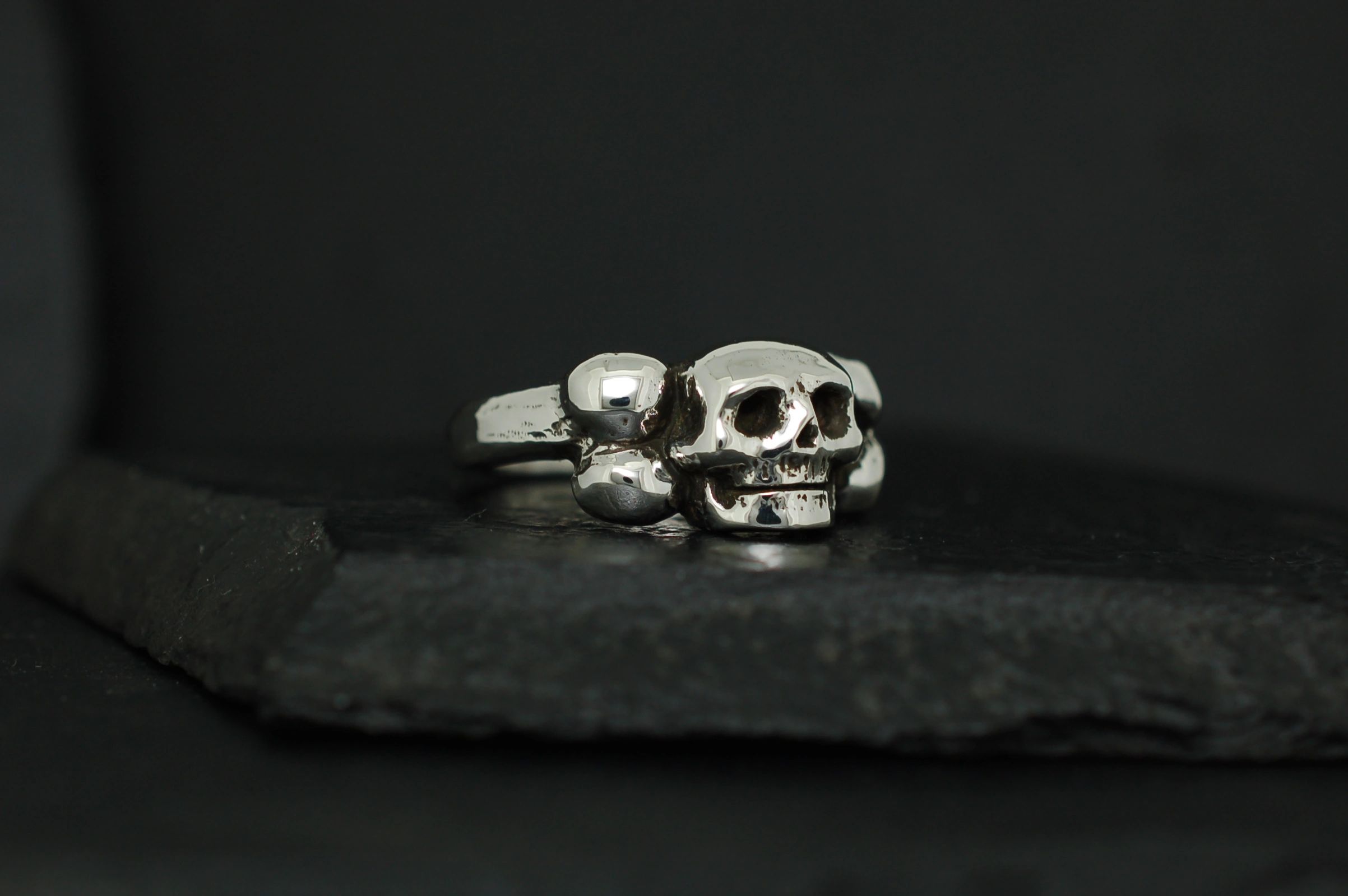 Two silver skull rings on a dark surface.