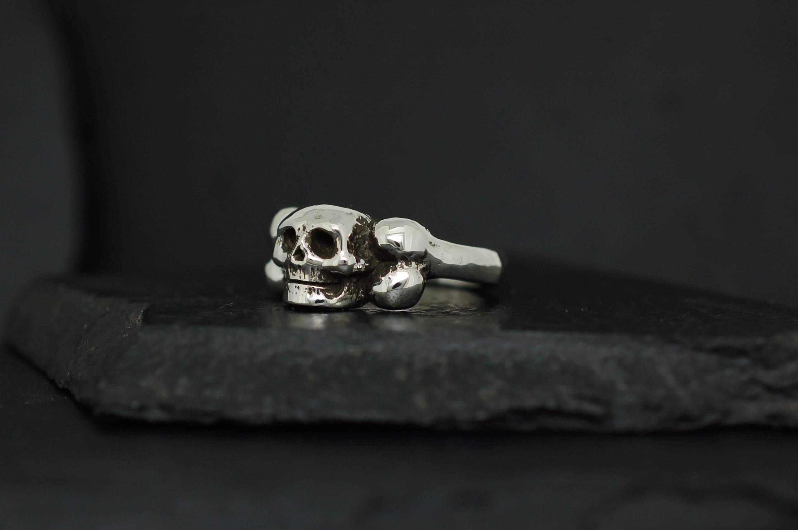 Silver skull ring on a dark surface.