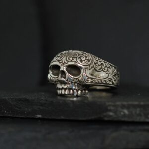 Intricately detailed skull ring with floral engravings on a dark background.