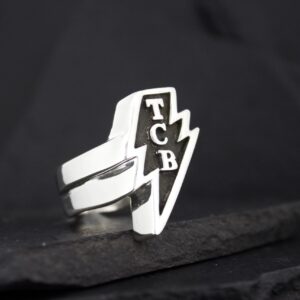 A silver ring with a lightning bolt and 'TCB' initials.