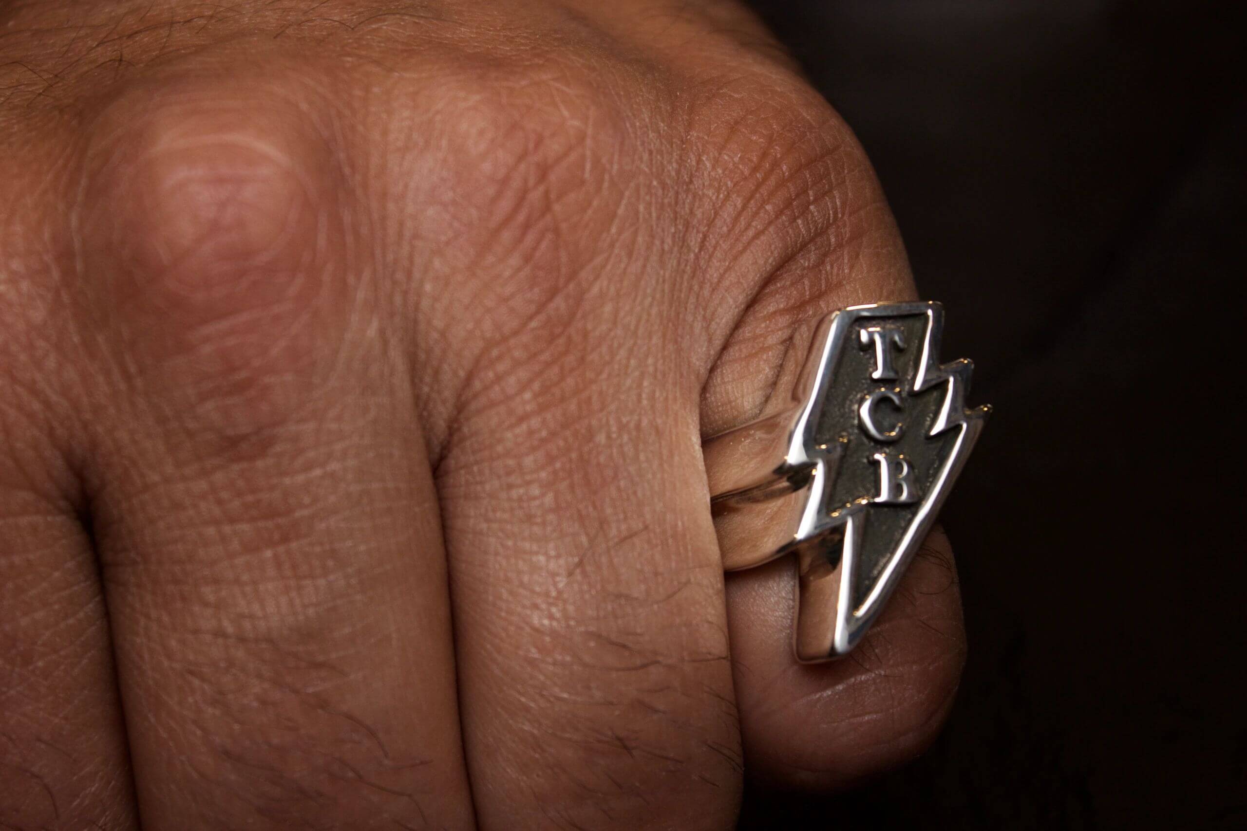 Close-up of a hand wearing a silver ring with the word 'FUCK' and a lightning bolt.