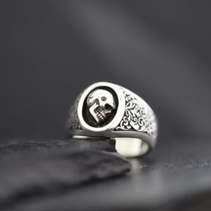 Silver ring with a skull emblem on a dark surface.
