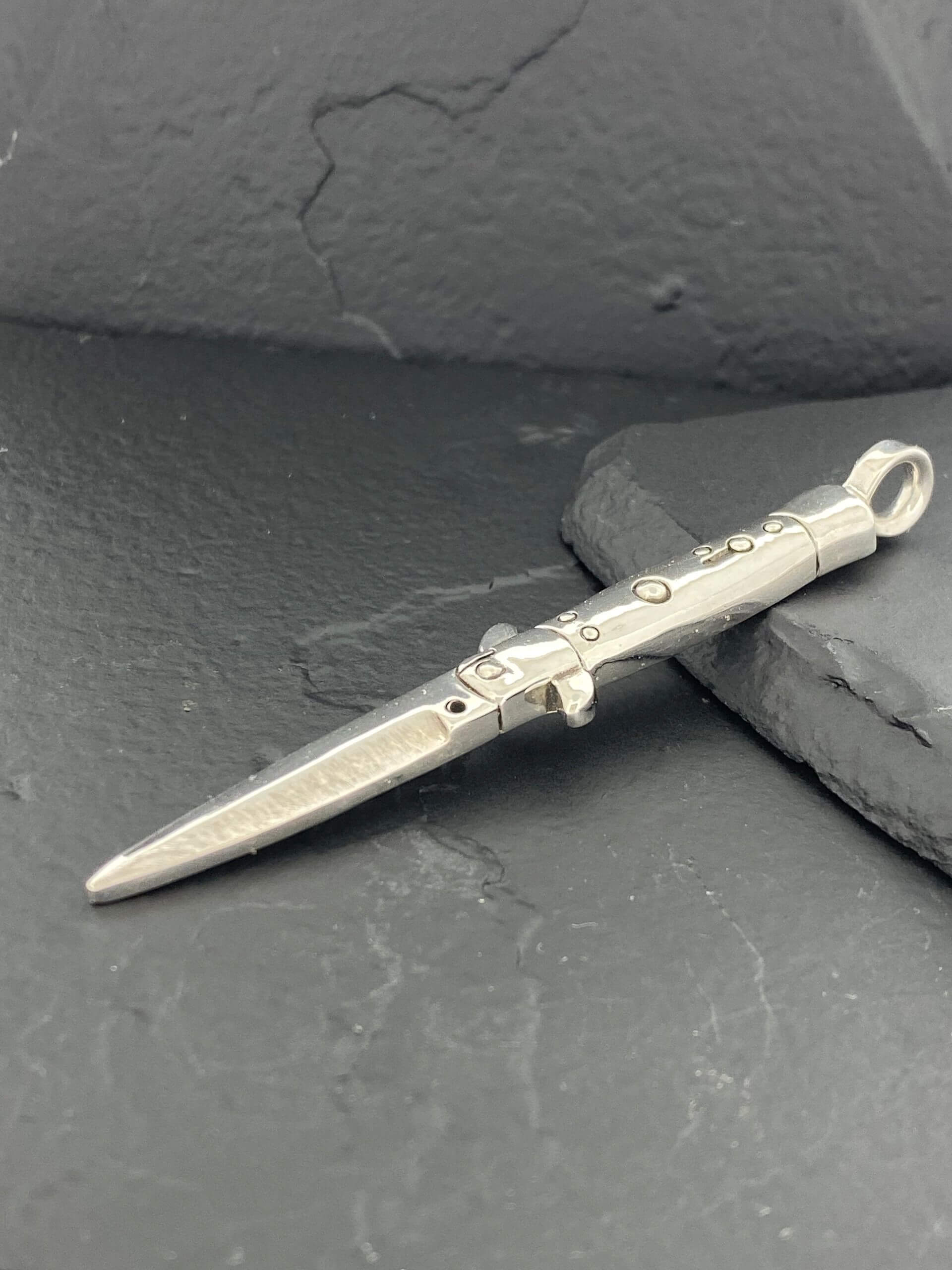 Small silver dagger pendant on a dark surface.