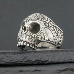 Intricately designed silver skull ring with ornate patterns.