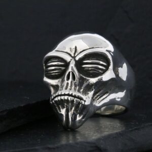 A metallic skull ring with intricate details on a dark background.