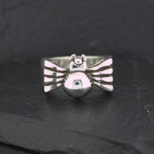 Silver bird-shaped ring with detailed wings on a black surface.