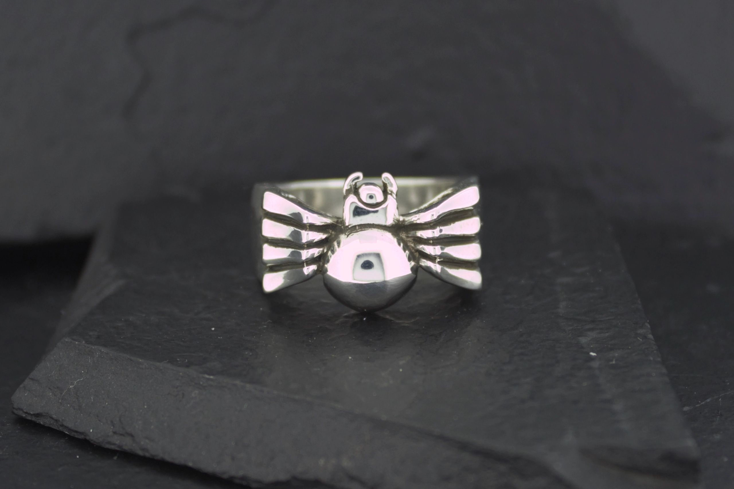 Silver bird-shaped ring with detailed wings on a black surface.