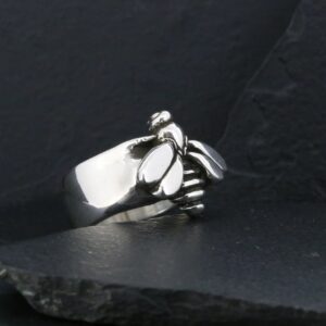 Silver ring shaped like a clenched fist on dark surface.