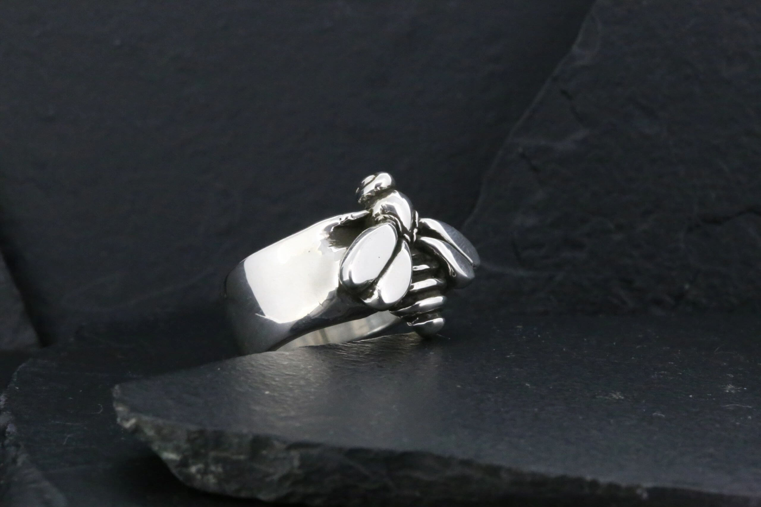 Silver ring shaped like a clenched fist on dark surface.