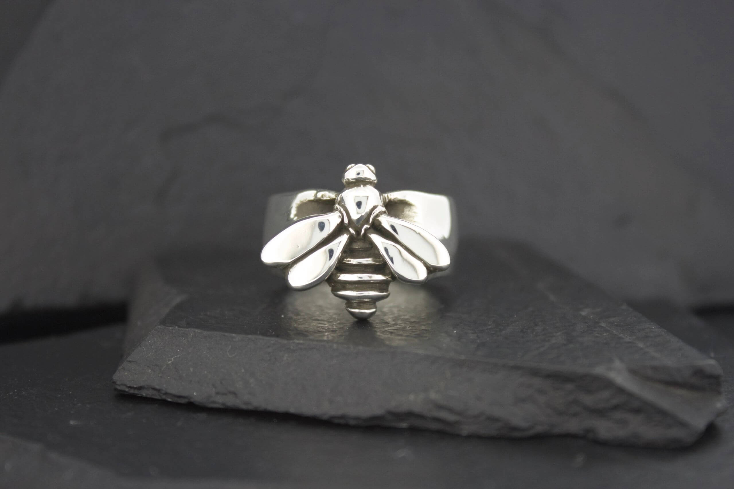 A silver bee-shaped ring on a dark stone surface.