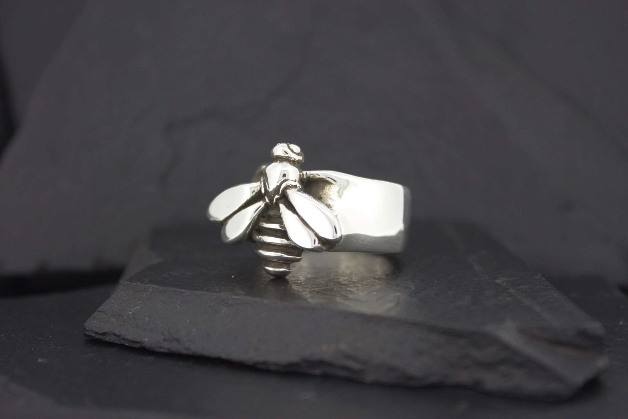 Silver bee-themed ring on a dark surface.