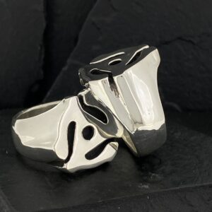 Glossy silver rings with unique abstract black designs on a black background.