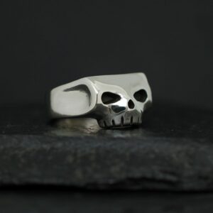 Silver skull-shaped ring on a dark surface.