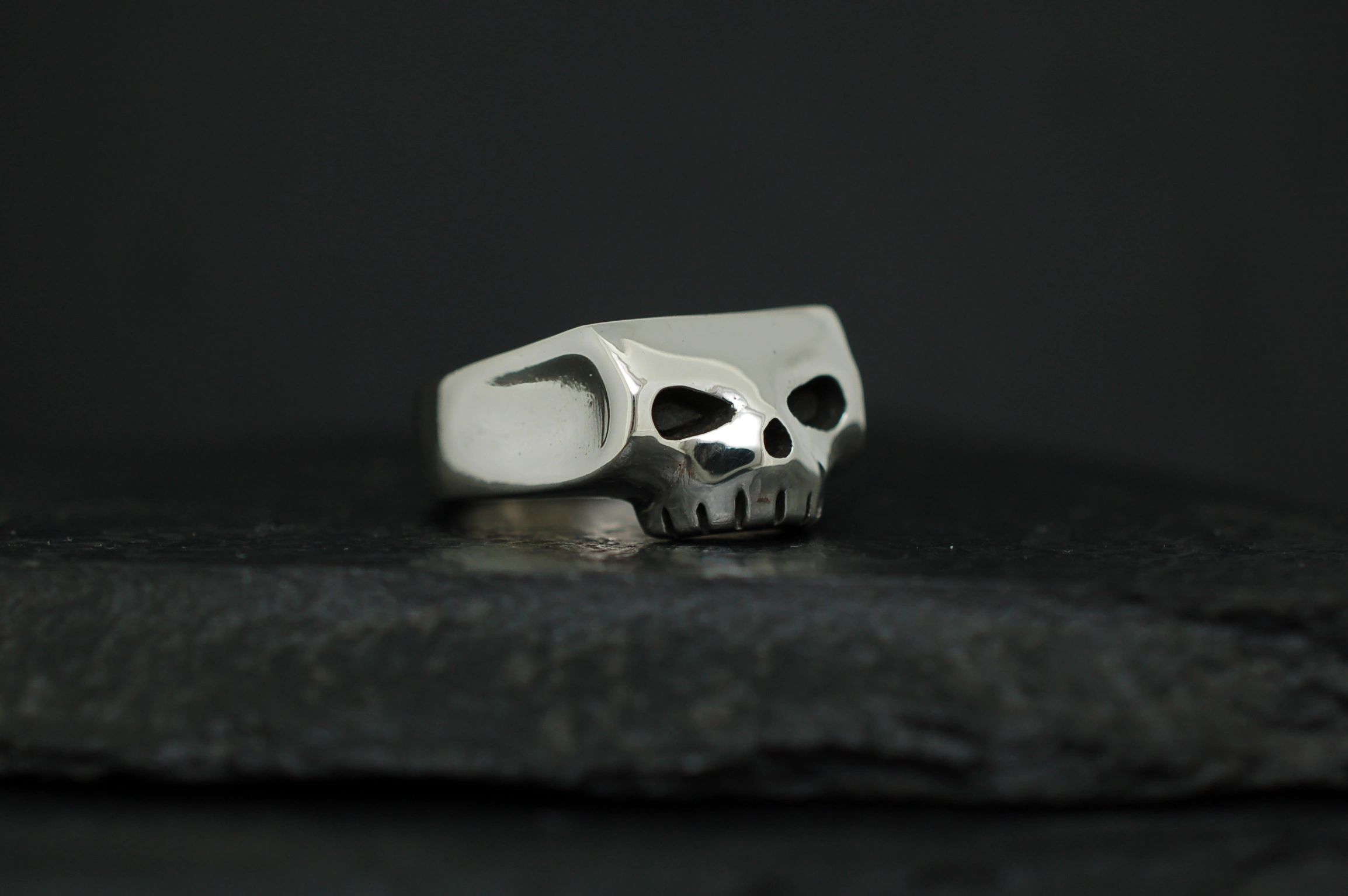 Silver skull-shaped ring on a dark surface.