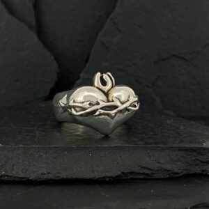 Silver ring with a heart and Om symbol on a dark stone background.