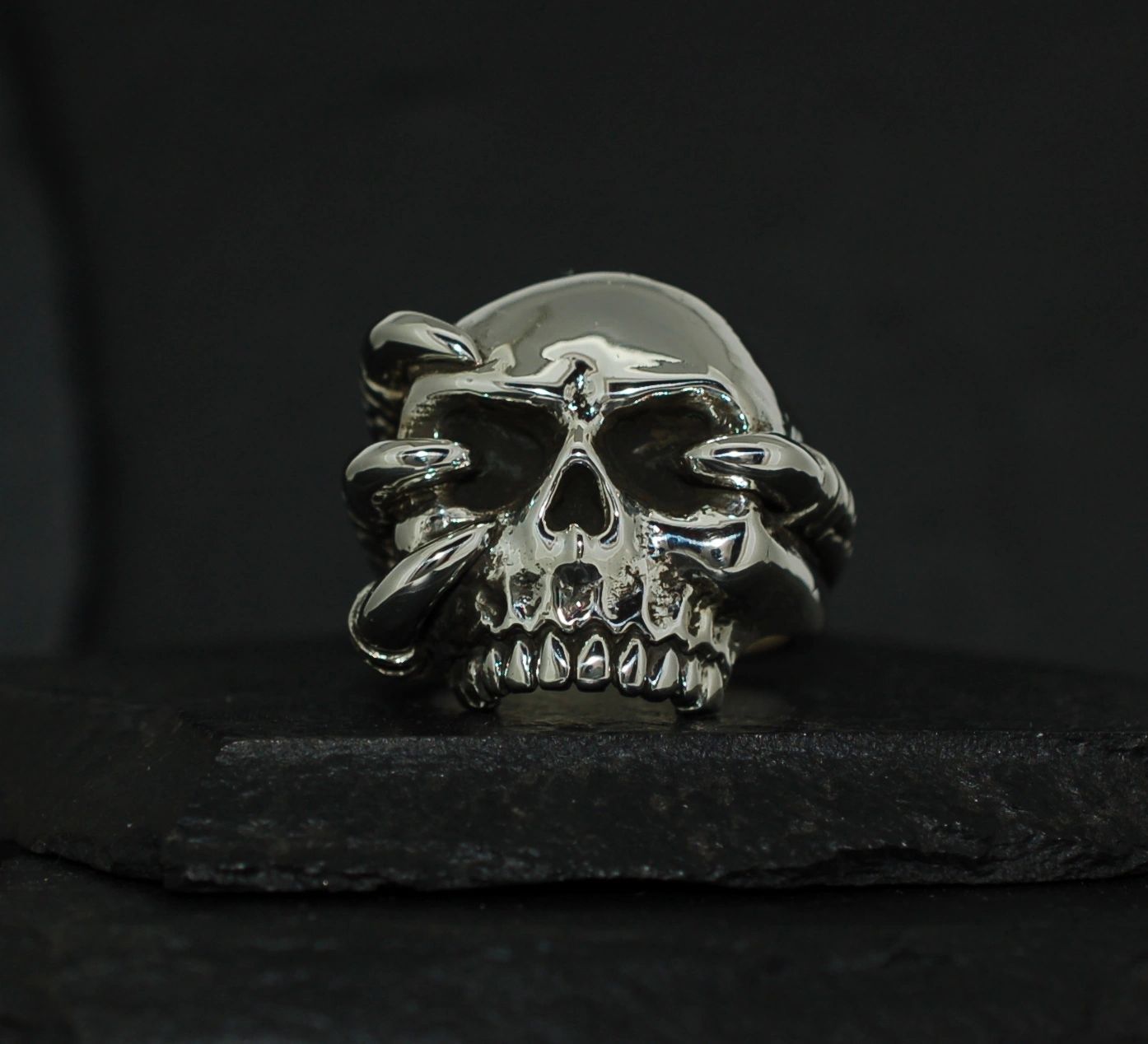 Metal skull ring with intricate serpent design on dark background.