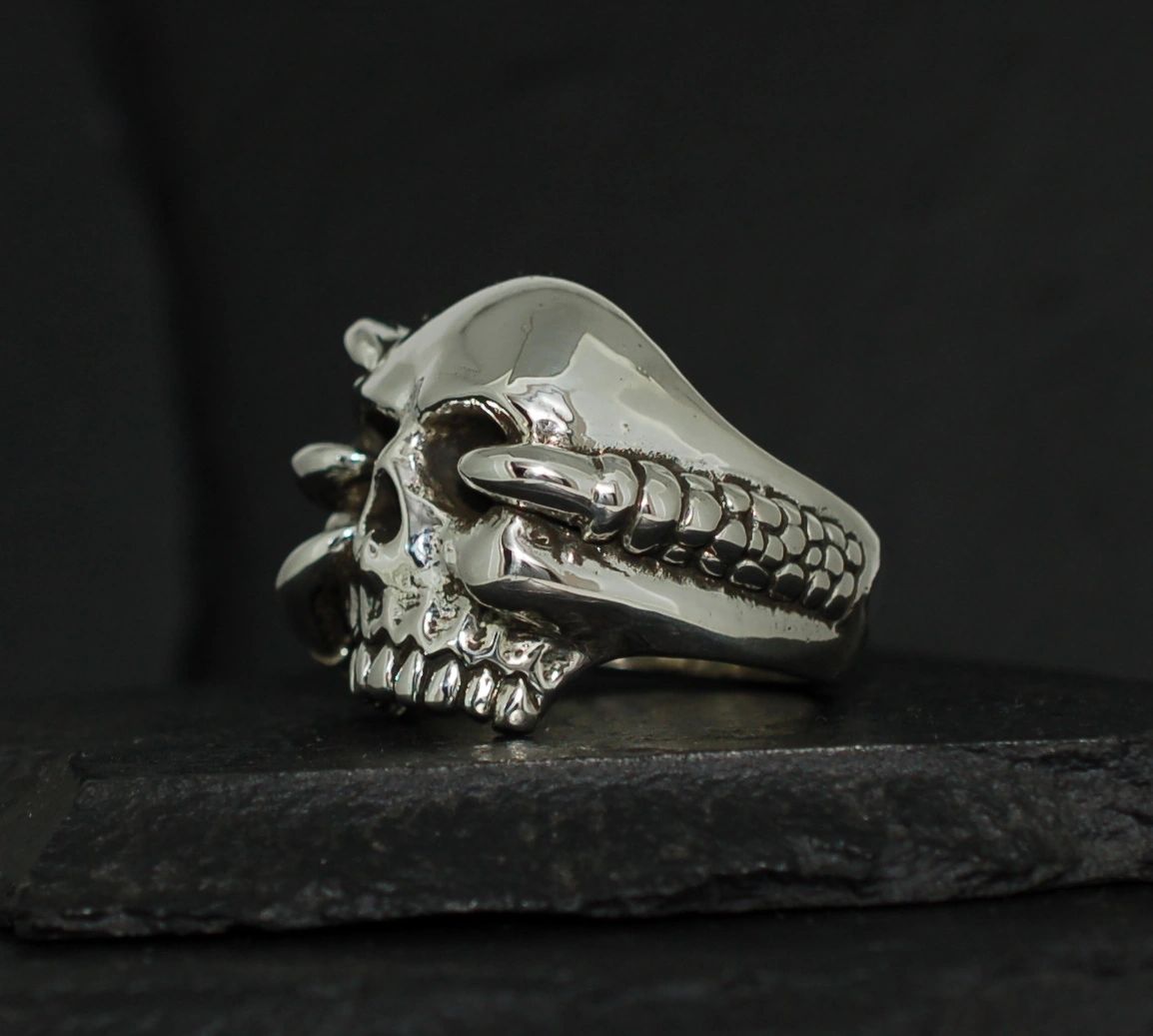 A silver skull ring with detailed teeth and eye sockets on a black background.