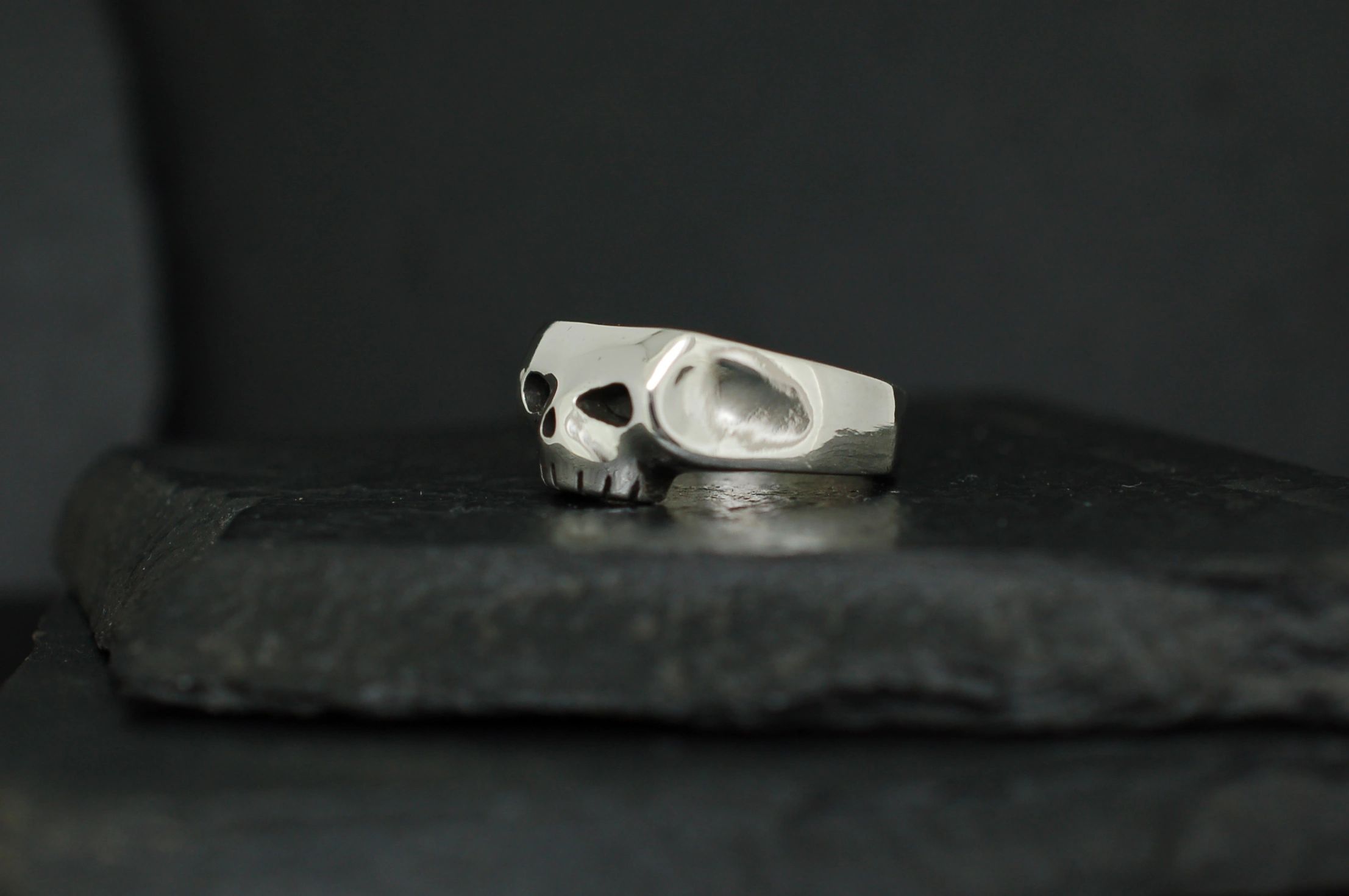 A silver ring featuring a skull design on a dark surface.