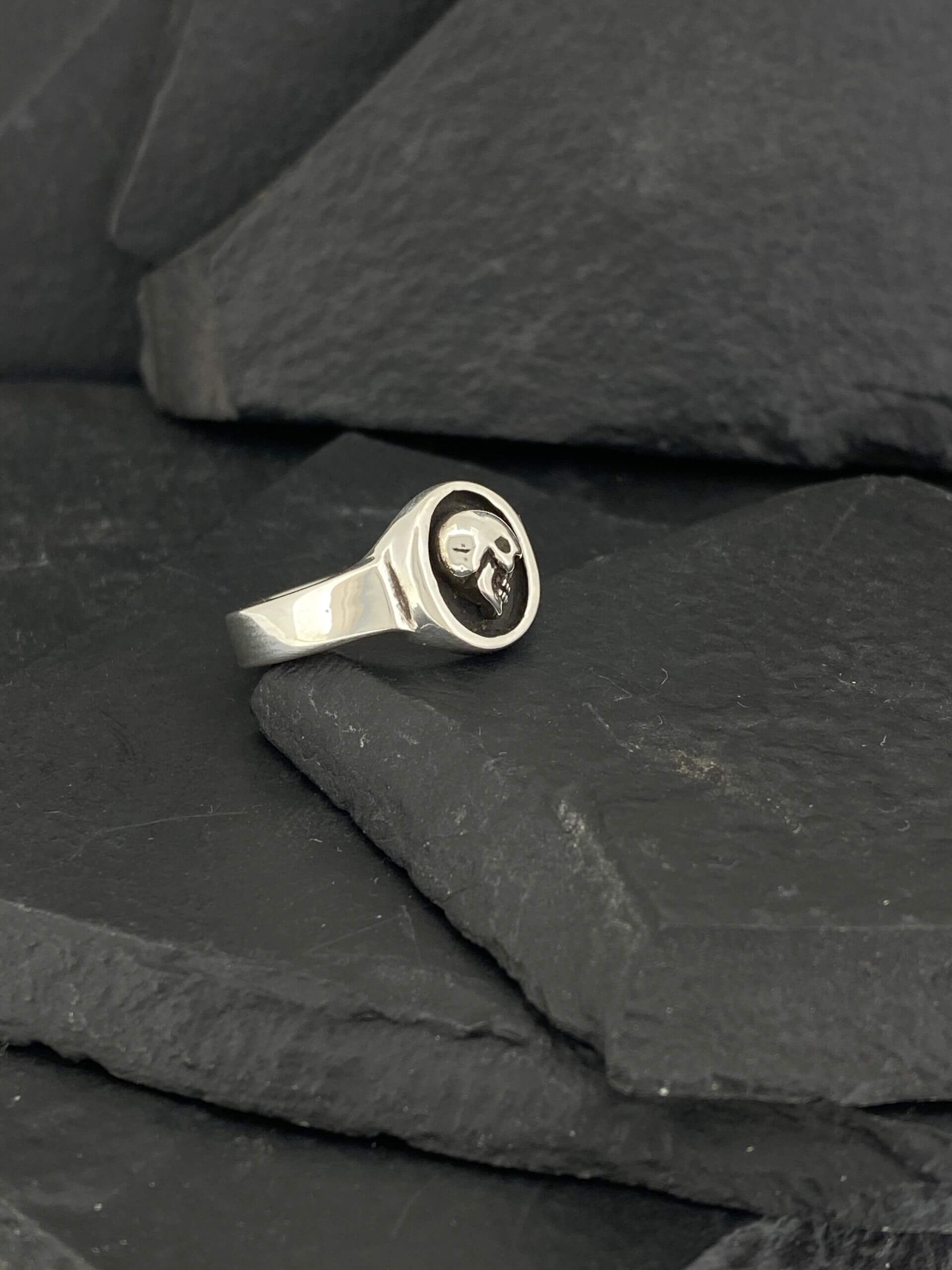Silver ring with a black skull emblem on slate stones.
