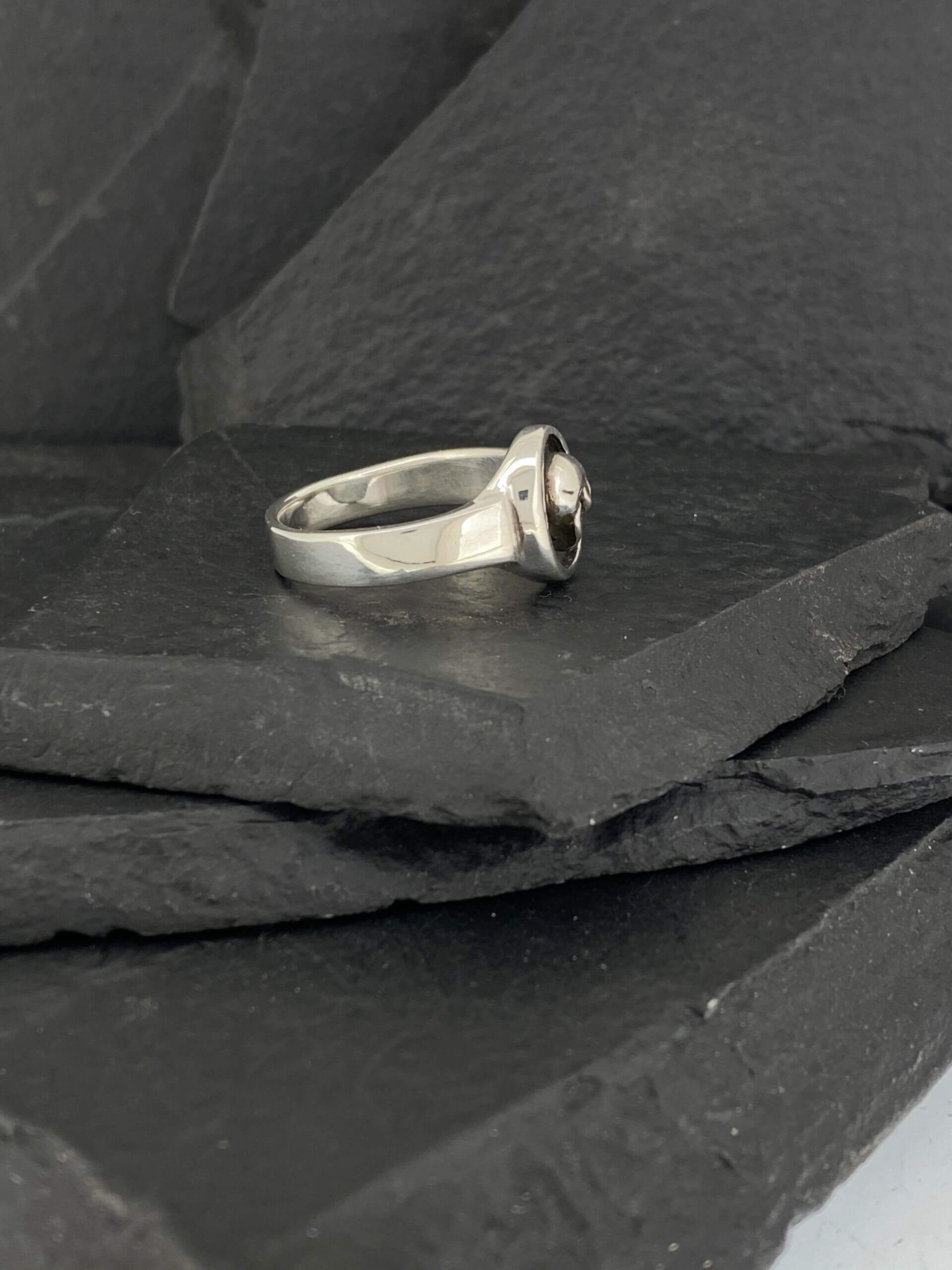 Elegant silver ring with a central gemstone on dark slate tiles.