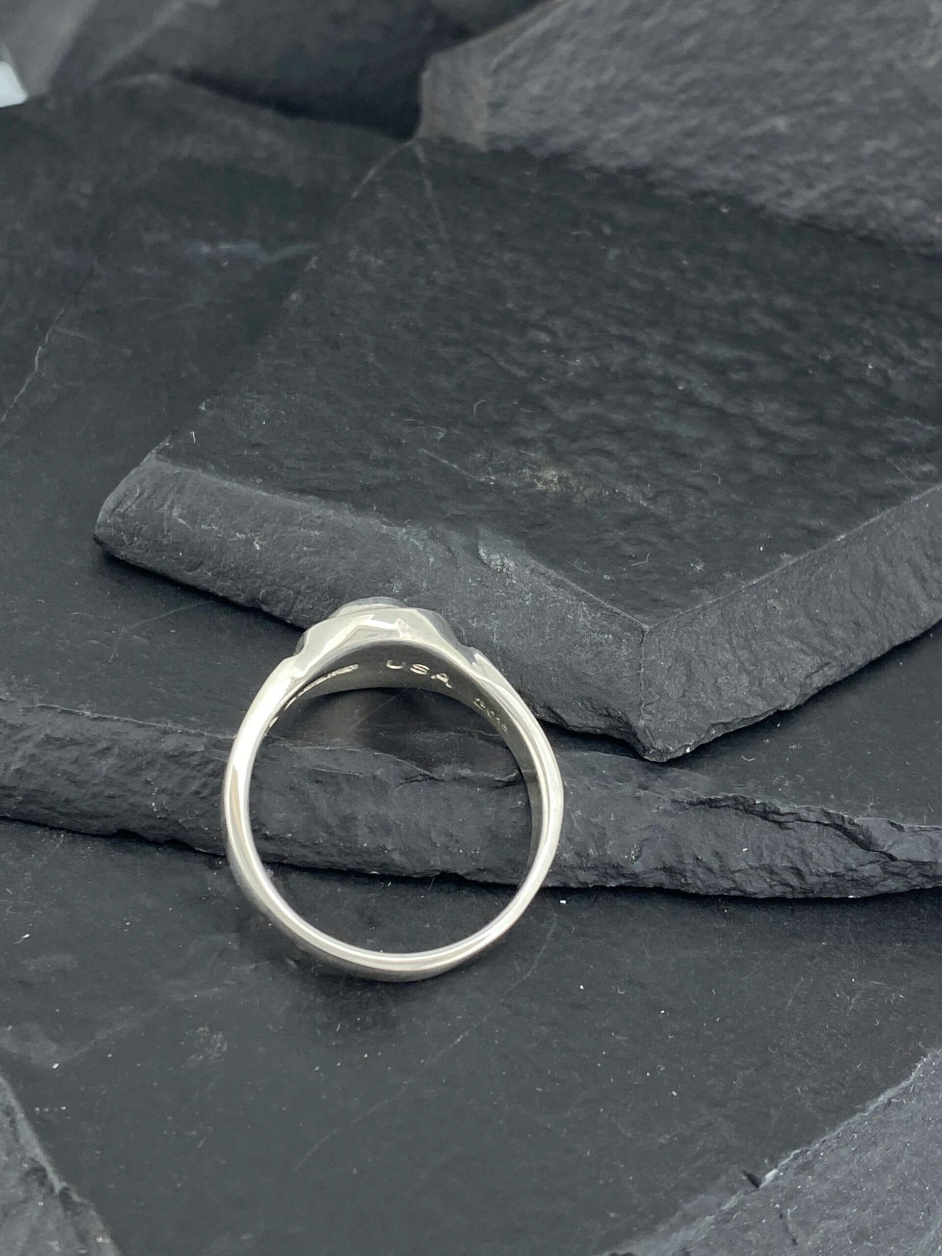 Elegant silver ring with a smooth design on a dark textured surface.