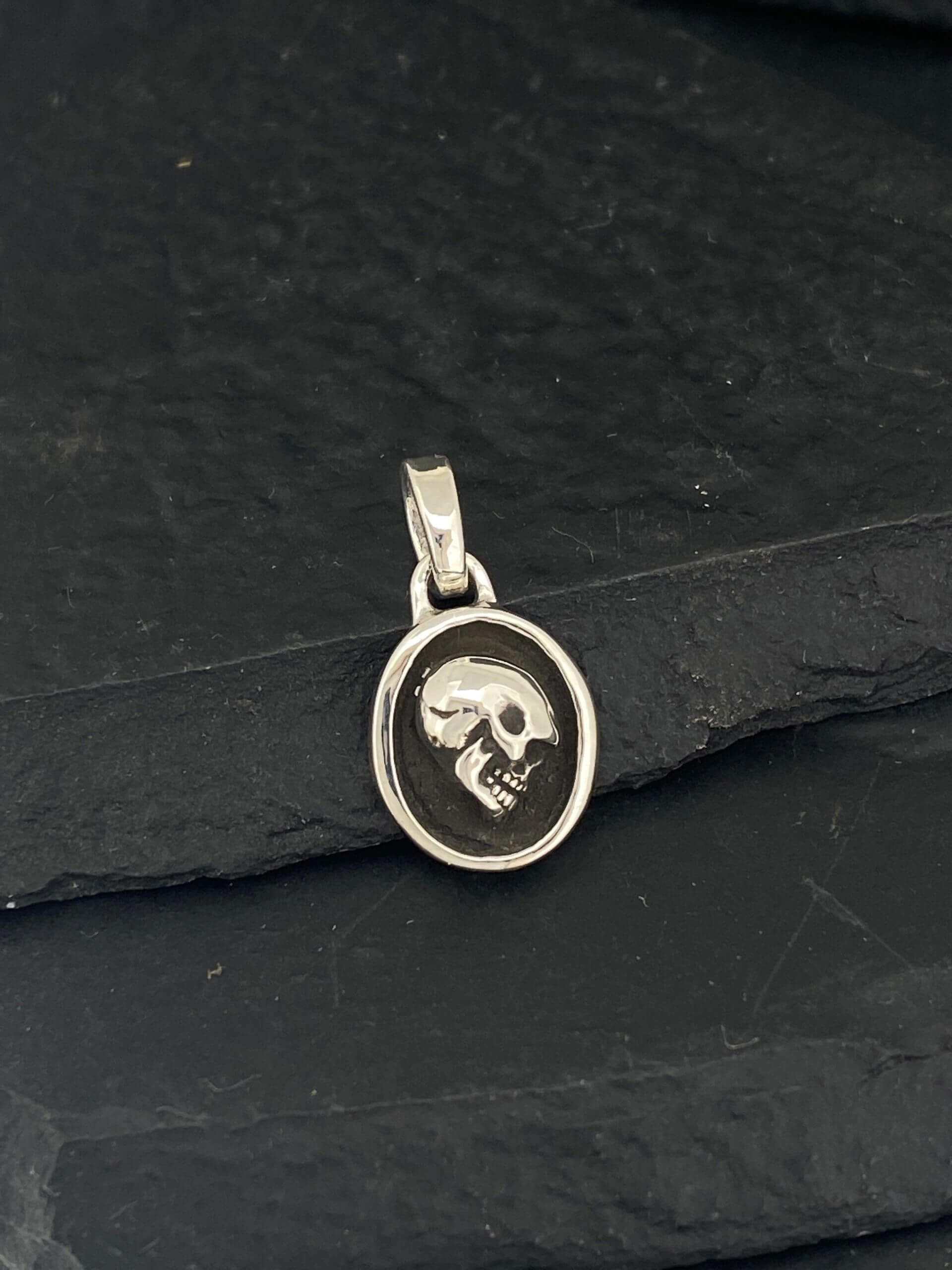 Oval silver pendant featuring a detailed skull design.