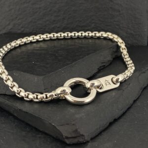 Elegant silver bracelet with a circular clasp on a dark textured surface.
