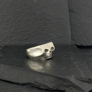 A silver skull ring on a dark textured surface.