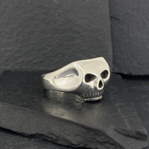 A silver skull ring resting on dark slate stones.