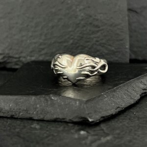 Elegant silver ring with an intricate, flowing design on a dark slate surface.