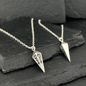 Two silver geometric pendant necklaces on a dark stone surface.