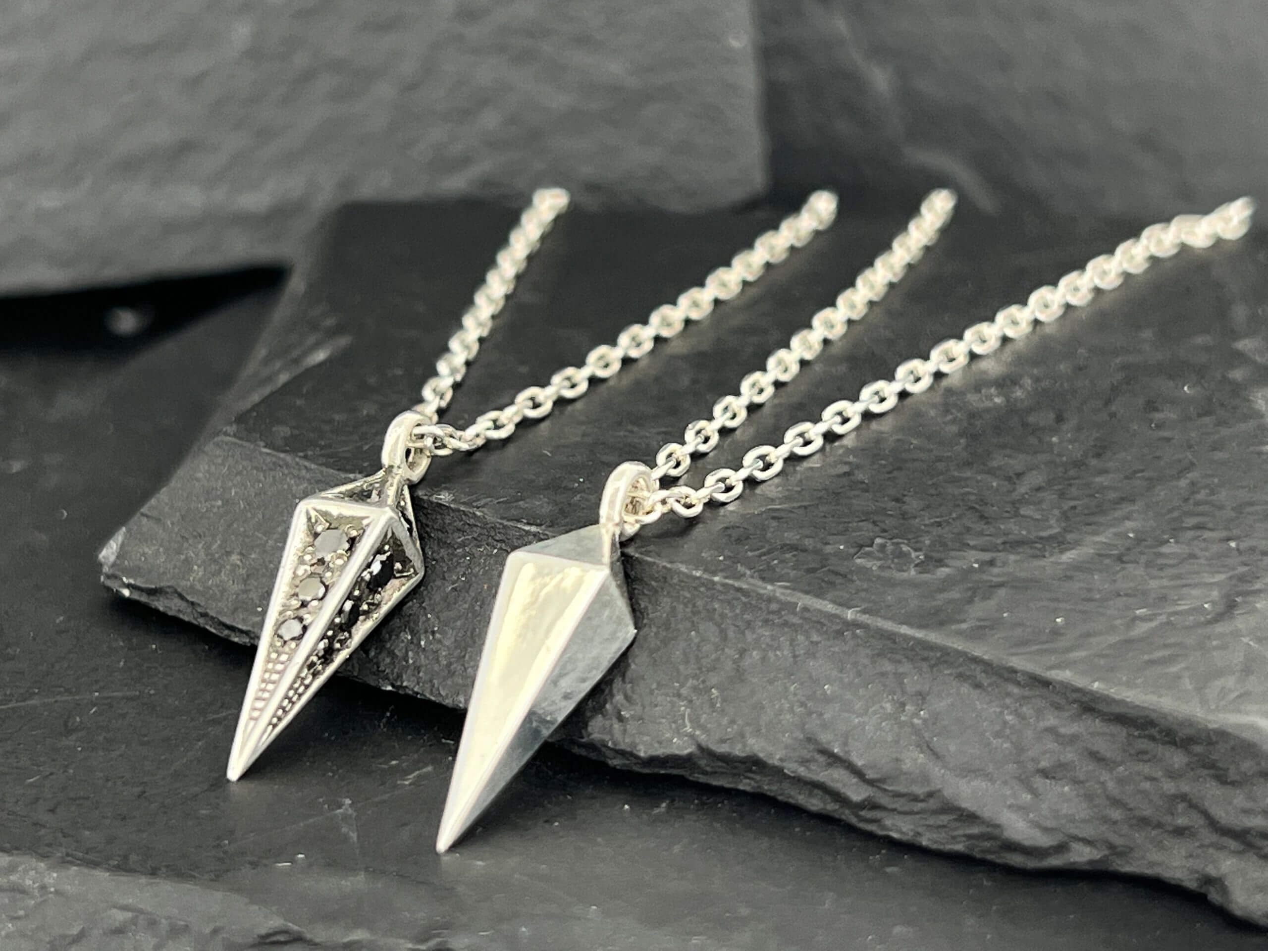 Two geometric pendant necklaces displayed on dark slate.