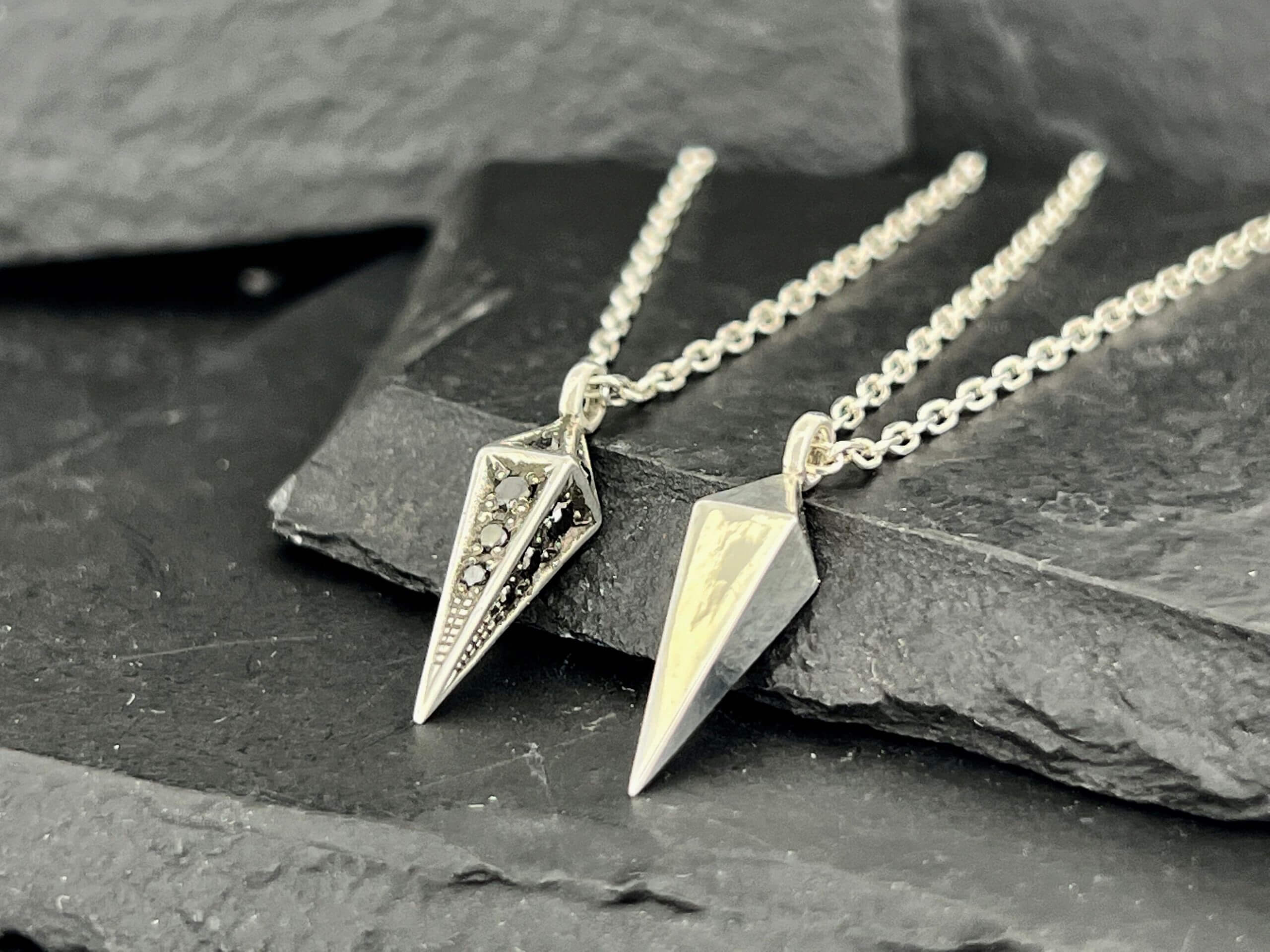 Two elegant silver arrowhead pendants on chains displayed on dark stone.