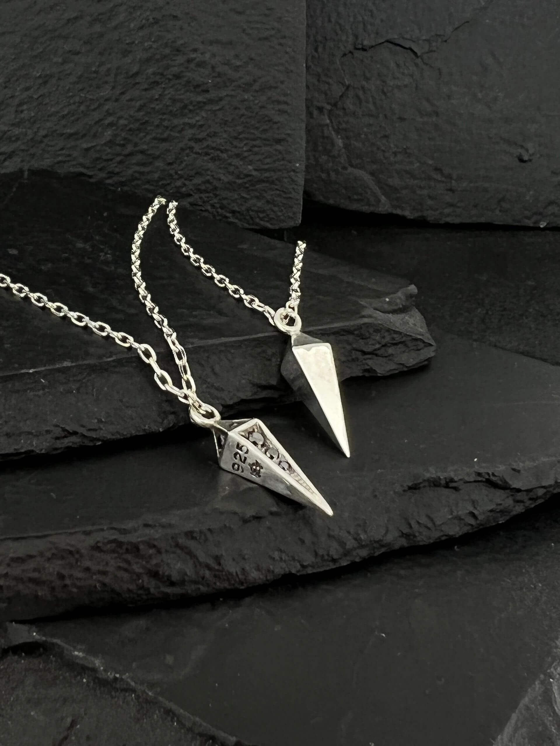 Two silver pendulums on chains placed on black slate.