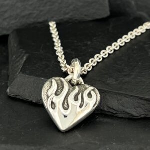 Silver heart pendant with flame design on chain.