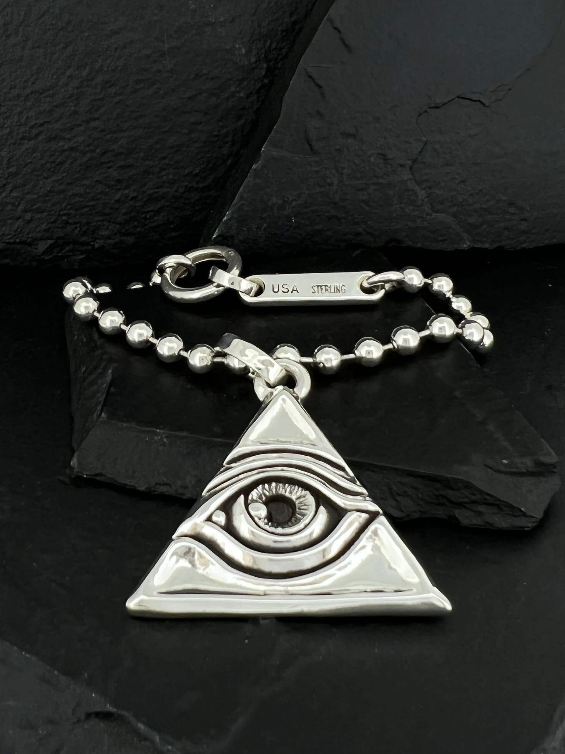 Silver pendant shaped like an eye within a triangle on a beaded chain.